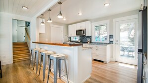 A modern kitchen with a central island, bar stools, white cabinetry, and a view to the outdoors.