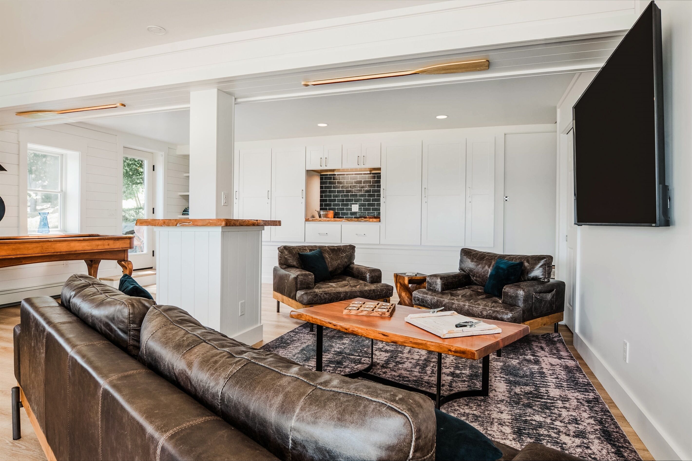 A modern living room with a brown leather sofa, two armchairs, a coffee table, and a piano in the background.