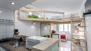 A modern kitchen with a built-in microwave, a sink, and a wooden loft bed with a green blanket.