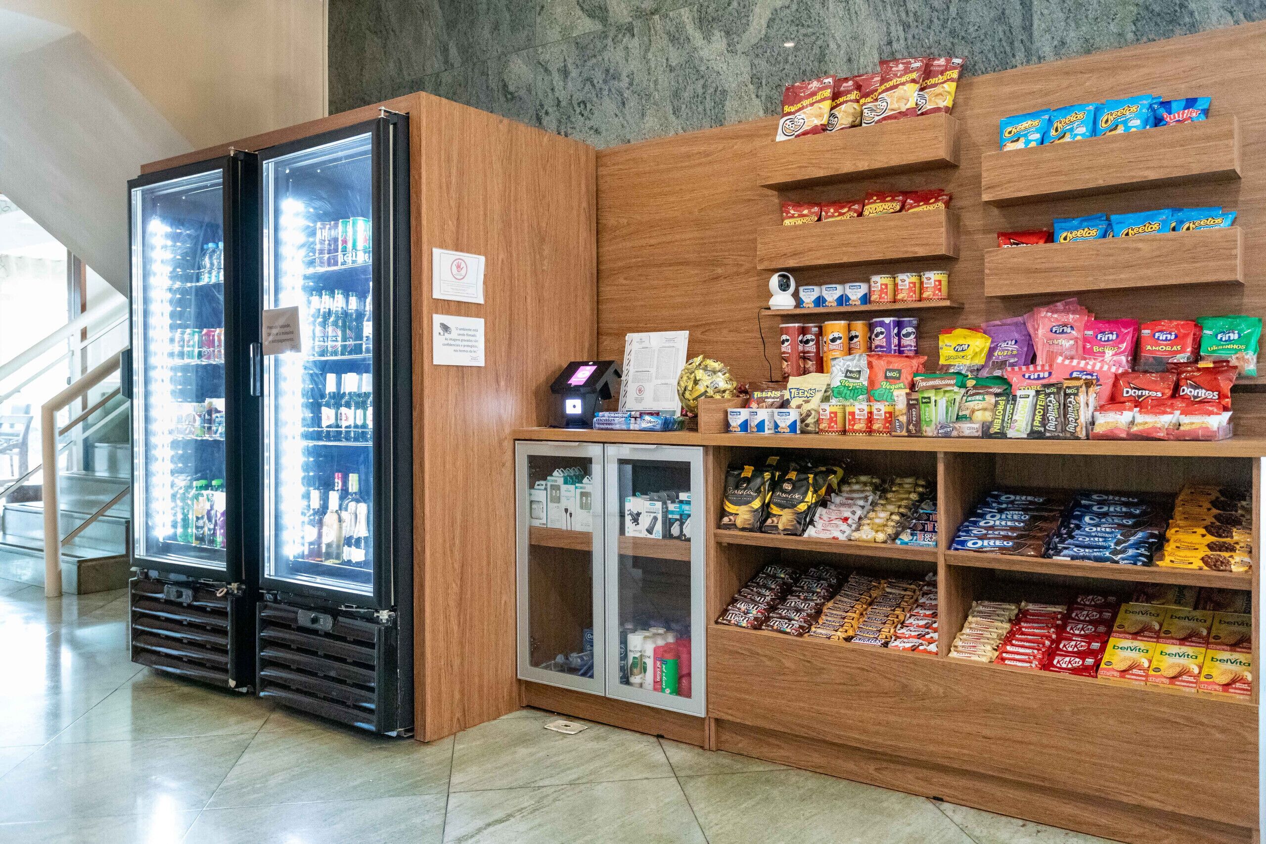 A refrigerated display case with snacks and beverages, a checkout counter, and a staircase in the background.
