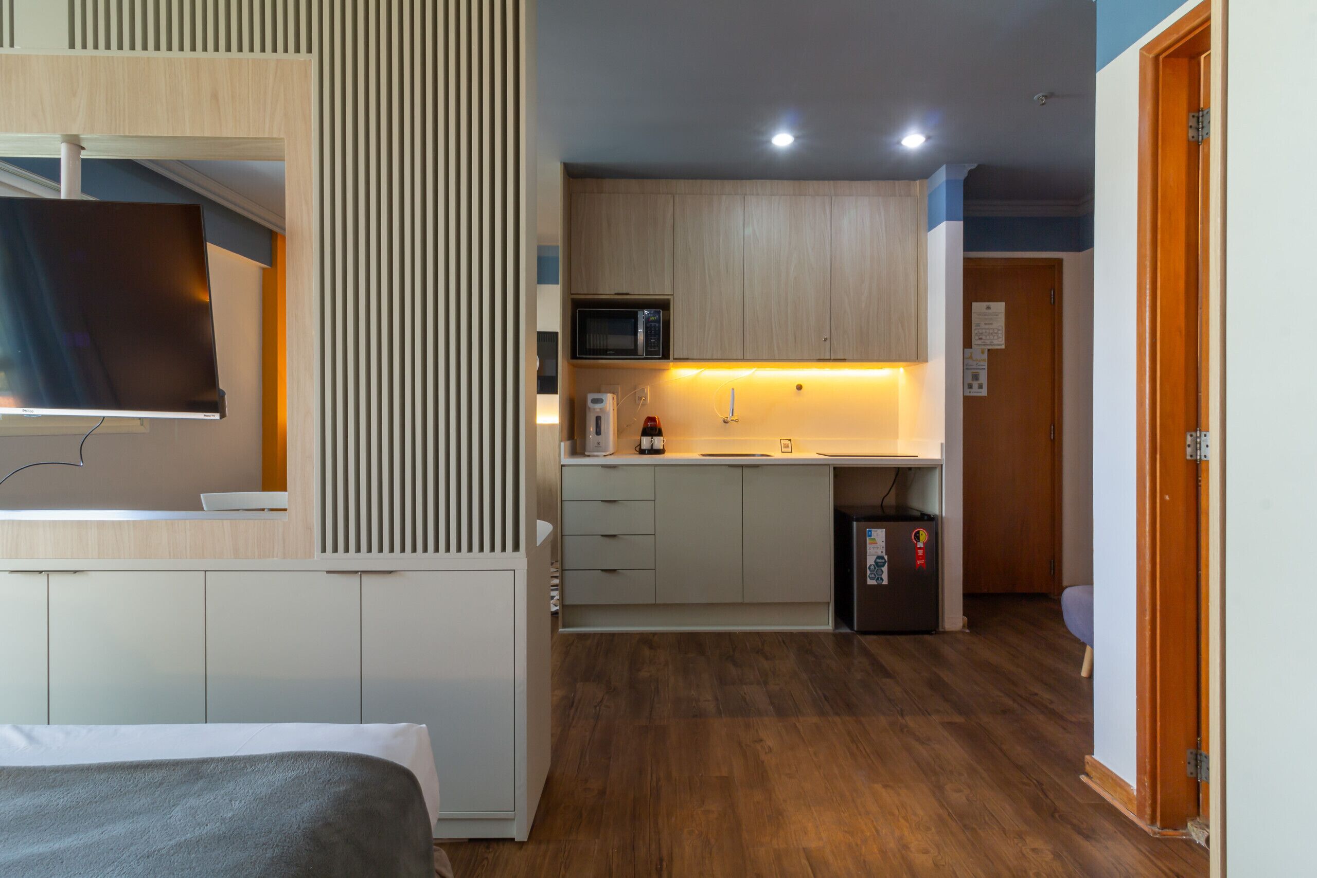 Ein kleines Hotelzimmer mit Bett, Fernseher, Küchenzeile und Holzboden.