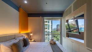 Habitación de hotel con una cama grande, un televisor en la pared y un balcón con vistas a la ciudad.