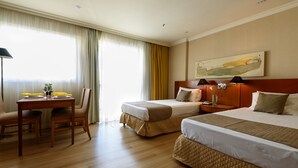 Une chambre d’hôtel avec deux lits, un bureau avec une chaise et une grande fenêtre avec des rideaux.