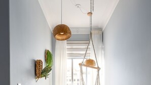 En gang med farverigt gulvtæppe, hængegyngestol og vægdekoration i fletværk.