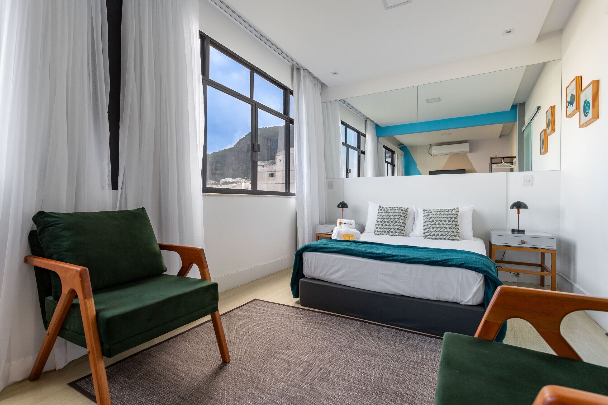 A modern hotel room with a bed, two chairs, a large window, and a mirror.