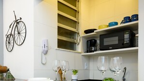 A modern kitchen with a black countertop, white and yellow tiles, a bicycle mounted on the wall, and two orange bar stools. - Peace in Copacabana | Forest view | BR1009 (Rio de Janeiro)