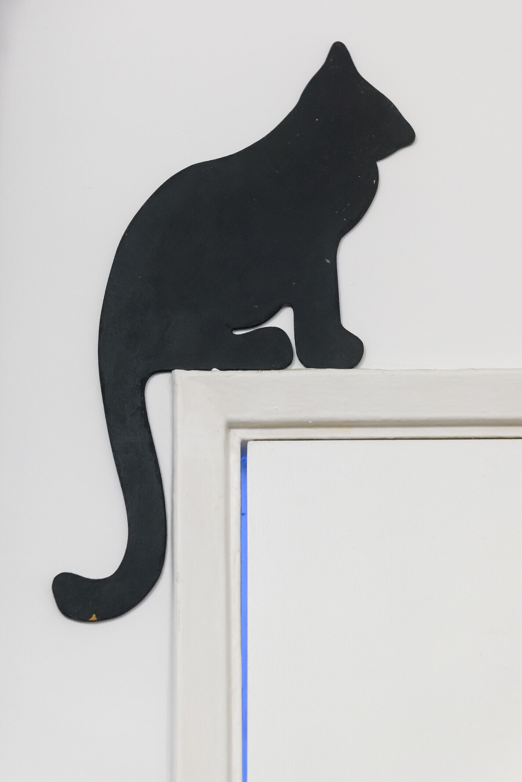 Silueta negra de un gato sobre una pared blanca.