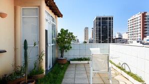 A rooftop patio with a white chair, potted plants, and a view of city buildings. - Penthouse in Ipanema | Christ View | MQC502 (Rio de Janeiro)