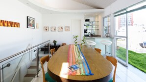A modern dining area with a wooden table, chairs, and a colorful runner. A staircase with glass railings leads to an upper level. - Penthouse in Ipanema | Christ View | MQC502 (Rio de Janeiro)