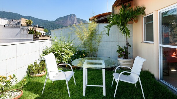 A glass-top table with white chairs in a small outdoor area with a view of a mountain. - Penthouse in Ipanema | Christ View | MQC502 (Rio de Janeiro)