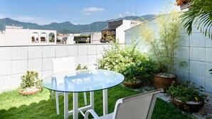 A rooftop terrace with a glass table and chairs, surrounded by potted plants and a view of distant mountains. - Penthouse in Ipanema | Christ View | MQC502 (Rio de Janeiro)