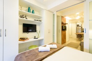 A modern hotel room with a bed, a TV, a desk with a chair, and a kitchenette. - Side sea view, 3min from the beach | PJ204 (Rio de Janeiro)