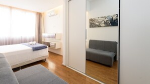 Et moderne hotelværelse med en seng, en grå sofa, et lille bord og et skab med skydedør.