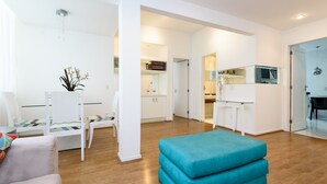 En moderne stue med sofa, en turkis puf og et spiseområde med bord og stole.