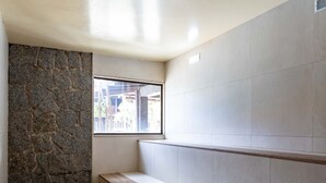 A corner of a room with a stone wall, a window, and a bench. - Apart Hotel  | BUZ215 (Armação dos Búzios)