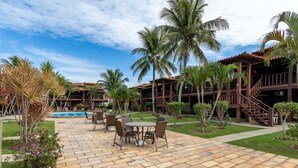 A resort with a pool, outdoor seating, palm trees, and a stone patio. - Apart Hotel  | BUZ215 (Armação dos Búzios)
