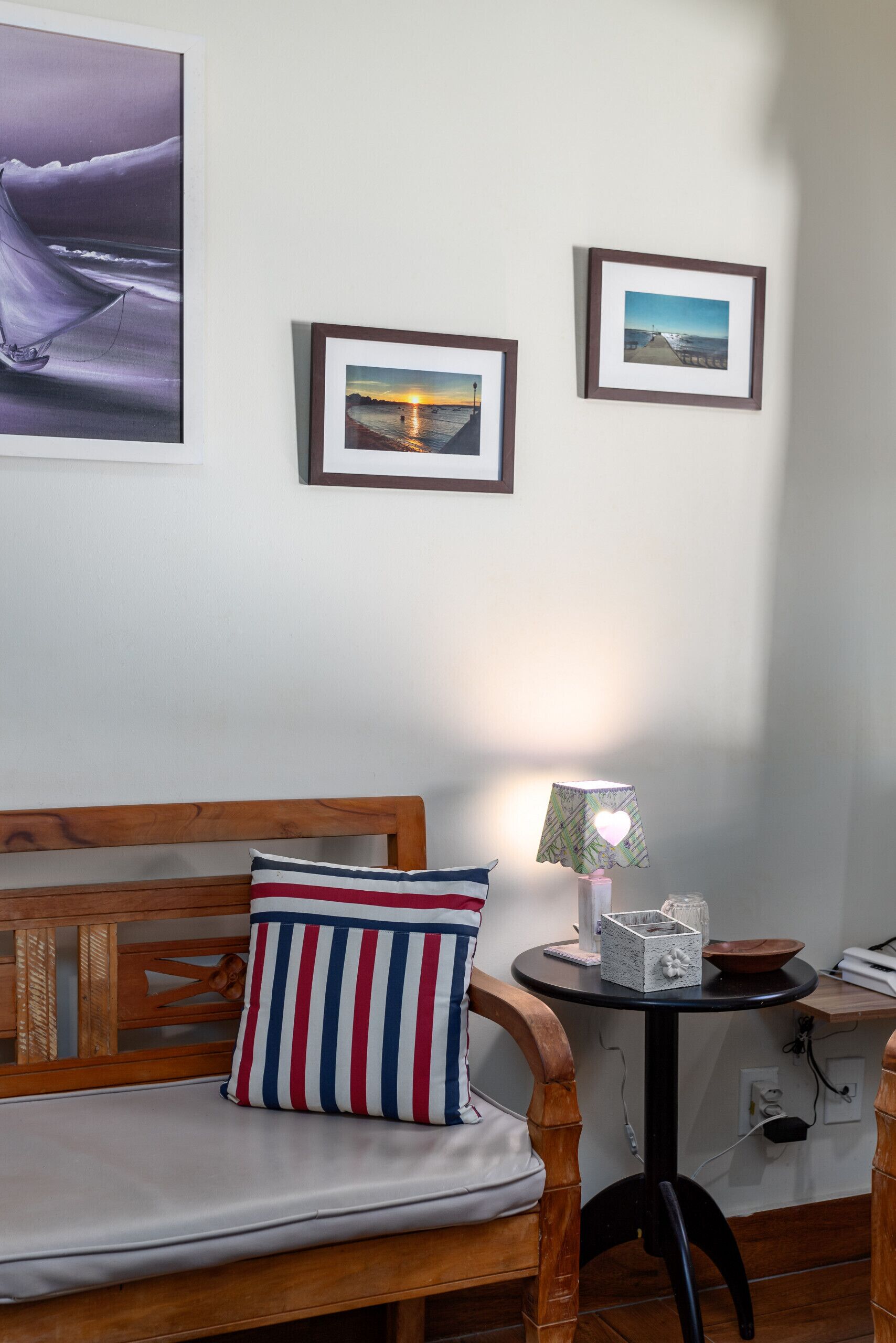 Ein gemütliches Zimmer mit einer hölzernen Bank, einem kleinen Tisch mit Lampe und gerahmten Bildern an der Wand.
