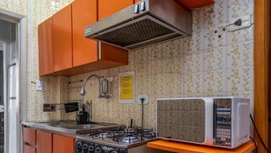A kitchen with orange cabinets, a gas stove, a microwave, and a white perforated shelf. - Style in Copacabana | Near the beach | BR403 (Rio de Janeiro)