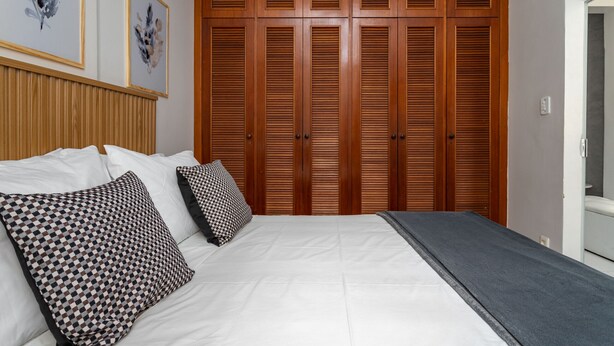 A bedroom with a large bed, wooden wardrobe, and two framed artworks on the wall. - Style in Copacabana | Near the beach | BR403 (Rio de Janeiro)