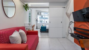 A modern hotel room with a red and white patterned sofa, a small desk, and a TV mounted on the wall.