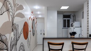A modern kitchen with white cabinets, a microwave, and a sink. There are two wooden stools at a small table.