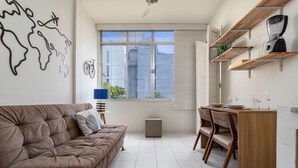 Ein modernes Wohnzimmer mit einem braunen Sofa, einem Esstisch mit Stühlen und einer Küchenzeile inklusive Mixer und Regalen.