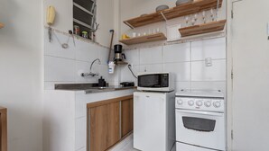 Eine kleine Küche mit Kühlschrank, Mikrowelle, Herd, Holzschränken und Regalen mit Geschirr und Gläsern.