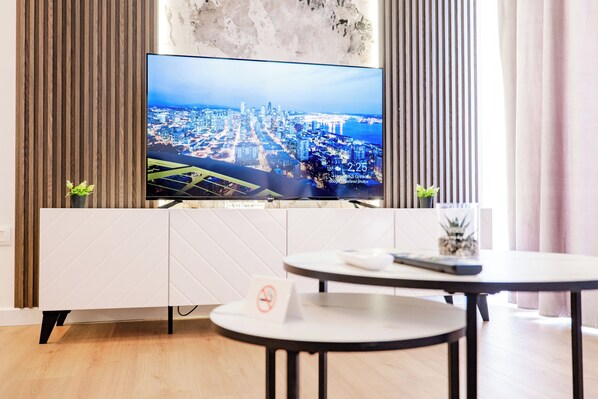 A modern room with a large TV displaying a cityscape, a white cabinet, a round table, and two small potted plants.