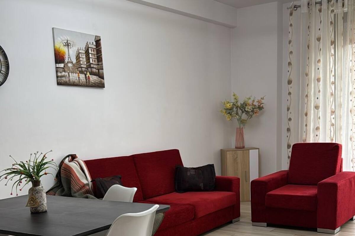 Un salon moderne avec un canapé rouge, une table à manger avec des chaises, un vase de fleurs et un tableau accroché au mur.