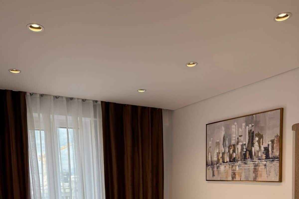 Une chambre d’hôtel avec un grand lit, un tableau représentant un paysage urbain accroché au mur et une fenêtre ornée de rideaux légers.