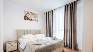 Une chambre à coucher avec un lit, une table de chevet, un tableau au mur et une fenêtre avec des rideaux.