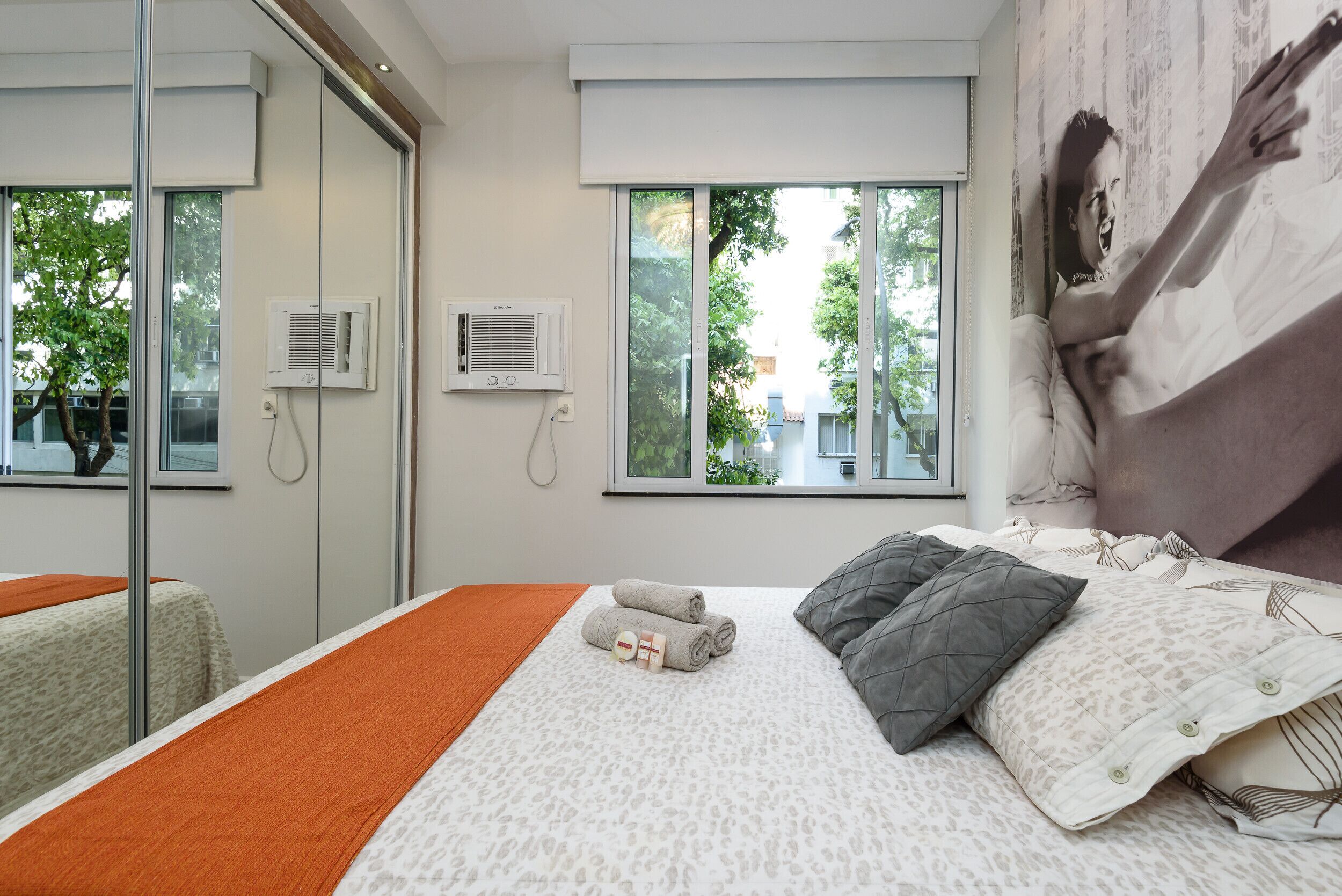 Quarto de hotel moderno com uma cama grande, uma porta de vidro e duas janelas.