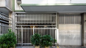 Una entrada protegida con barrotes de metal, plantas en macetas y una puerta metálica cerrada.
