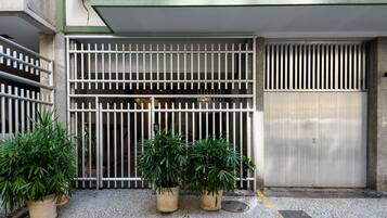 Uma entrada gradeada com barras de metal, plantas em vasos e uma porta de metal fechada.