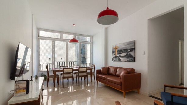 Ein geräumiges Wohnzimmer mit modernem Design, ausgestattet mit einem Ledersofa, einem Essbereich mit Holzsesseln und einem großen Fenster, das für natürliches Licht sorgt.