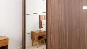 Ein Zimmer mit einem schiebbaren Holzschrank, einem Nachttisch aus Holz und einem Spiegel, der einen Teil des Raumes widerspiegelt.