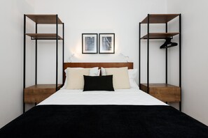 A bedroom with a bed, two wall-mounted shelves, and two framed pictures.
