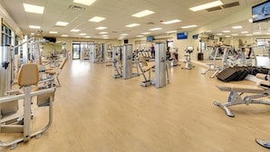 A spacious gym with various exercise machines, mirrors, and a television screen.
