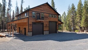 Une cabane en bois à deux étages, dotée d’un porche couvert, de deux portes de garage et d’une allée gravillonnée.