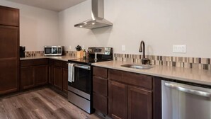 Une cuisine moderne avec des meubles en bois foncé, des appareils électroménagers en acier inoxydable, un four à micro-ondes, une cuisinière et un lave-vaisselle.