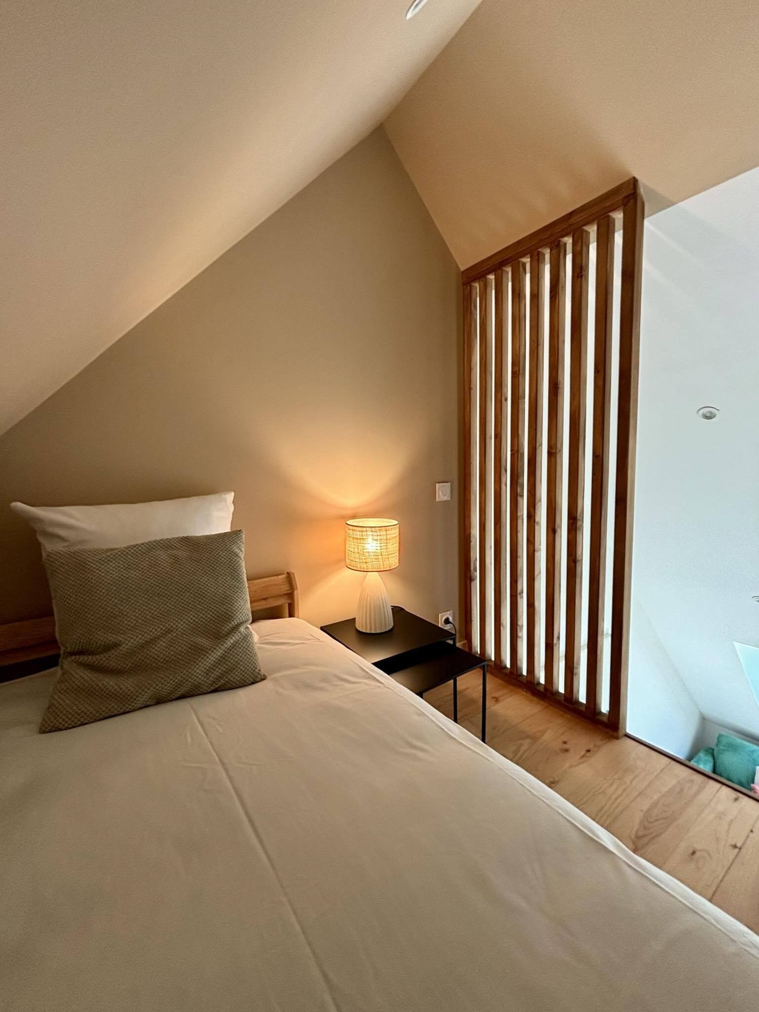 A bedroom with a bed, a nightstand, a lamp, and a wooden slat partition.