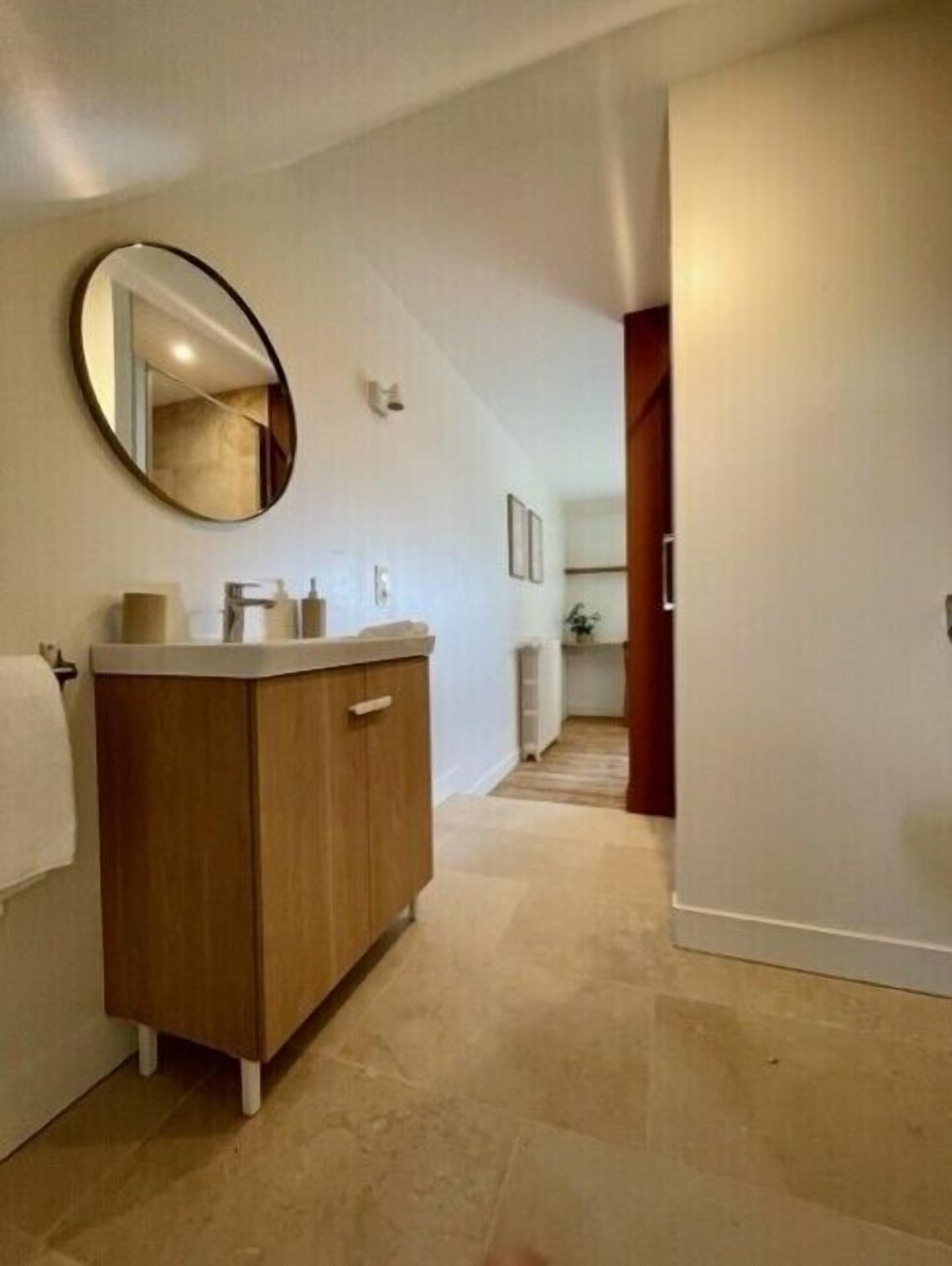 Une salle de bain moderne avec un meuble-lavabo en bois, un miroir rond et un sol carrelé.