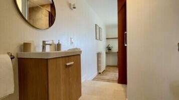 Une salle de bain moderne avec un meuble-lavabo en bois, un miroir rond et un sol carrelé.