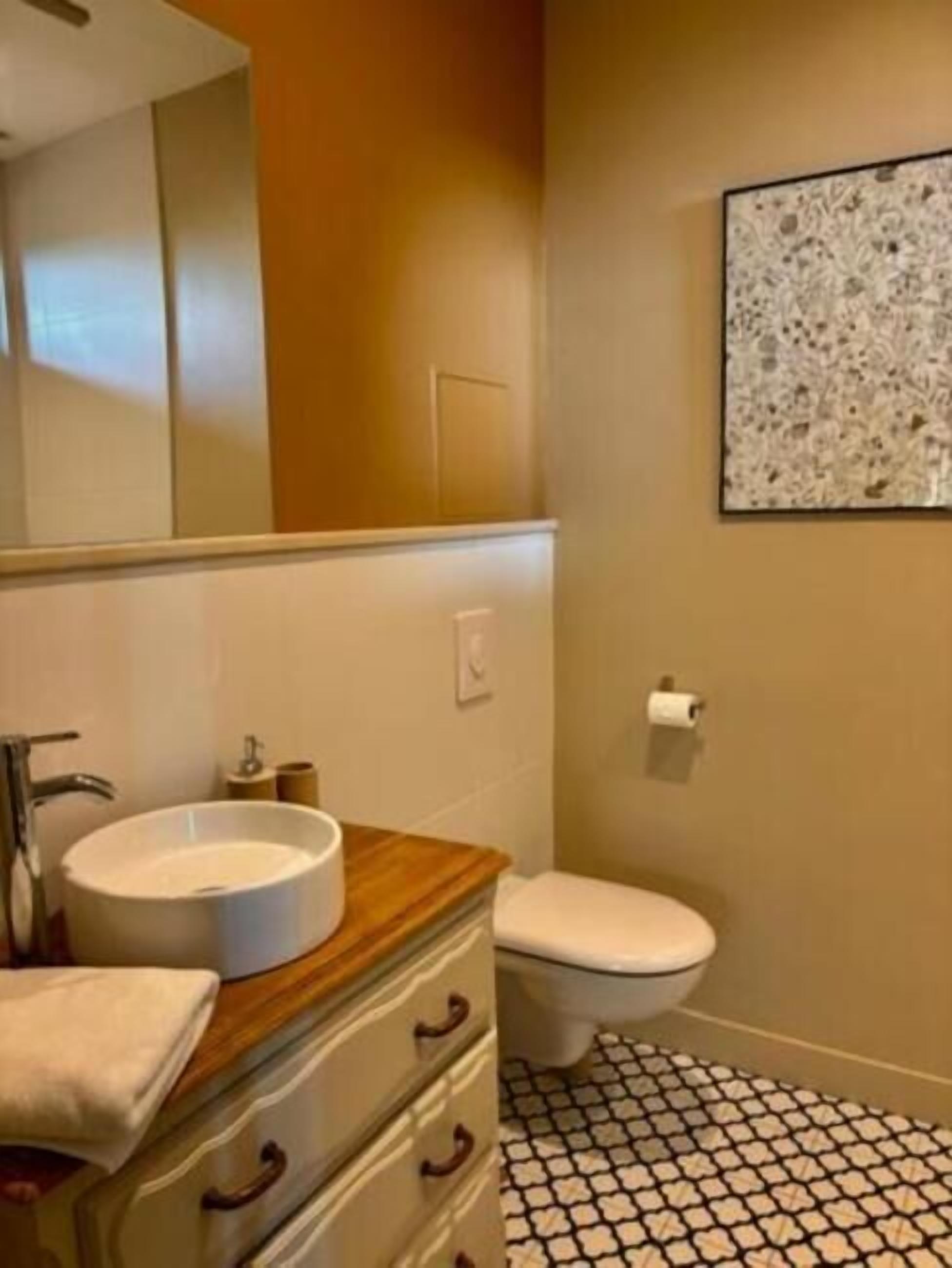 Un baño con un lavabo redondo, tocador de madera, inodoro y suelo estampado.