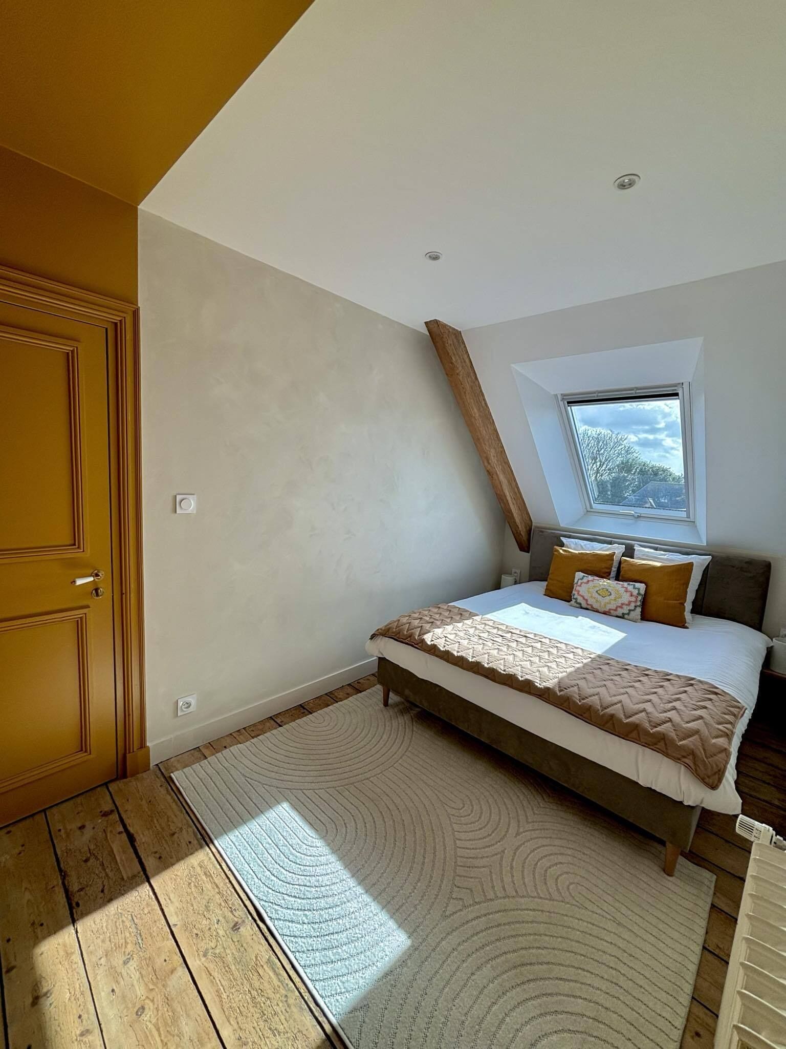 A bedroom with a sloped ceiling, a skylight, a bed with a patterned bedspread, and a wooden floor.