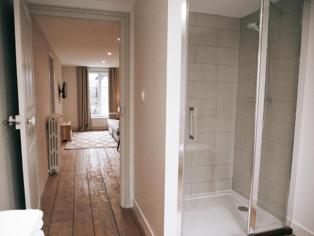 A hallway leading to a bathroom with a glass shower enclosure.