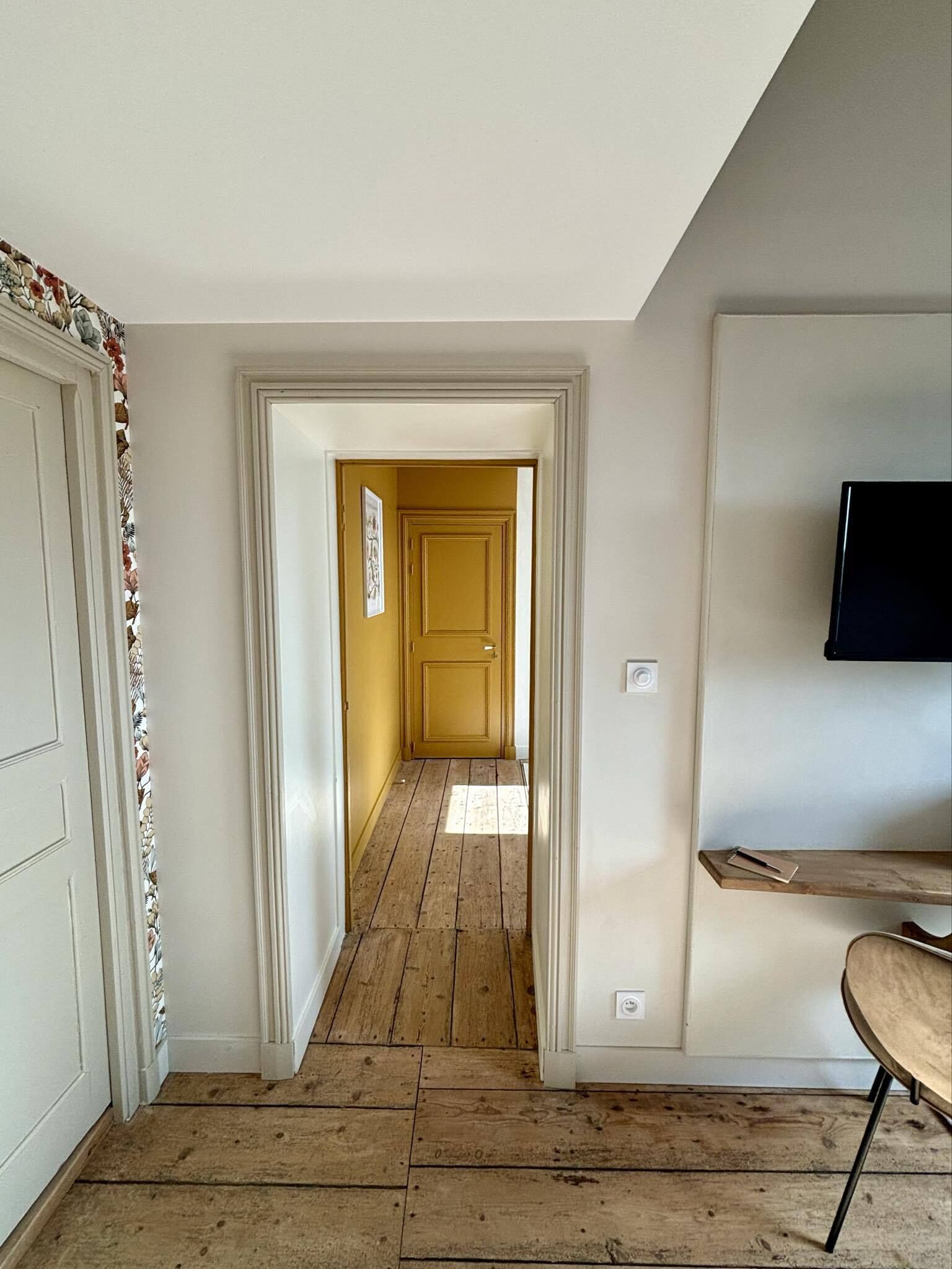 A hallway with wooden flooring, a white door on the left, and a yellow door at the end.