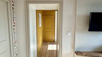 A hallway with wooden flooring, a white door on the left, and a yellow door at the end.