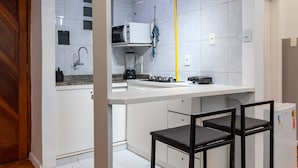 A compact kitchen with white cabinets, a microwave, a sink, and a small refrigerator. There are two black stools at the kitchen counter.