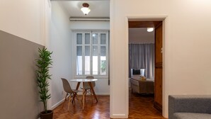 A hallway with a dining area, a potted plant, and a grey sofa.